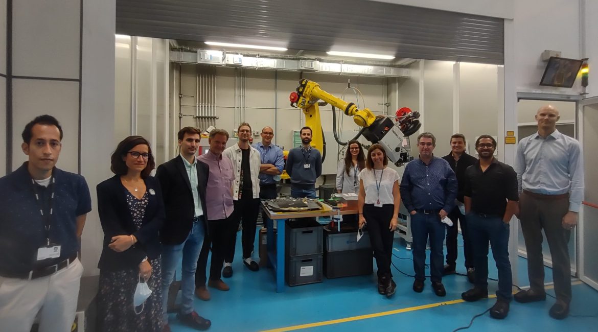 Photograph of the CAELESTIS team on a tour of AIMEN in Spain during the project Kick-Off Meeting on 9th May 2022, standing in front of a robot arm designed for manufacturing